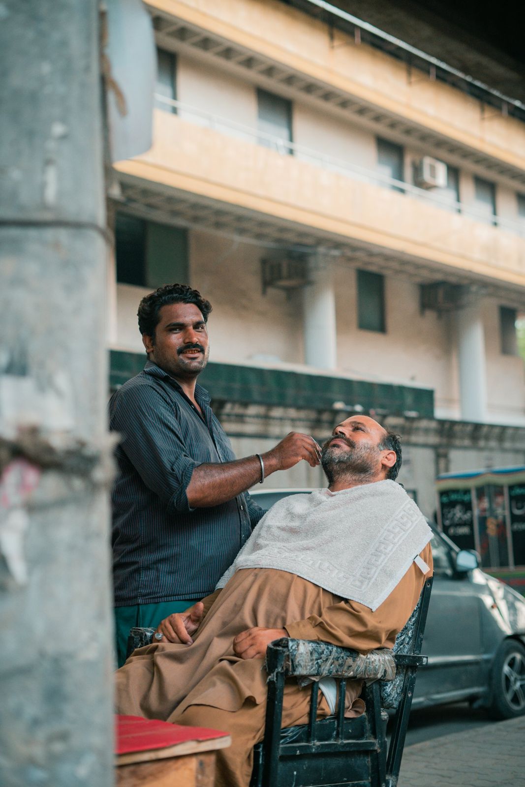 A barber shaving a customer at a roadside chair